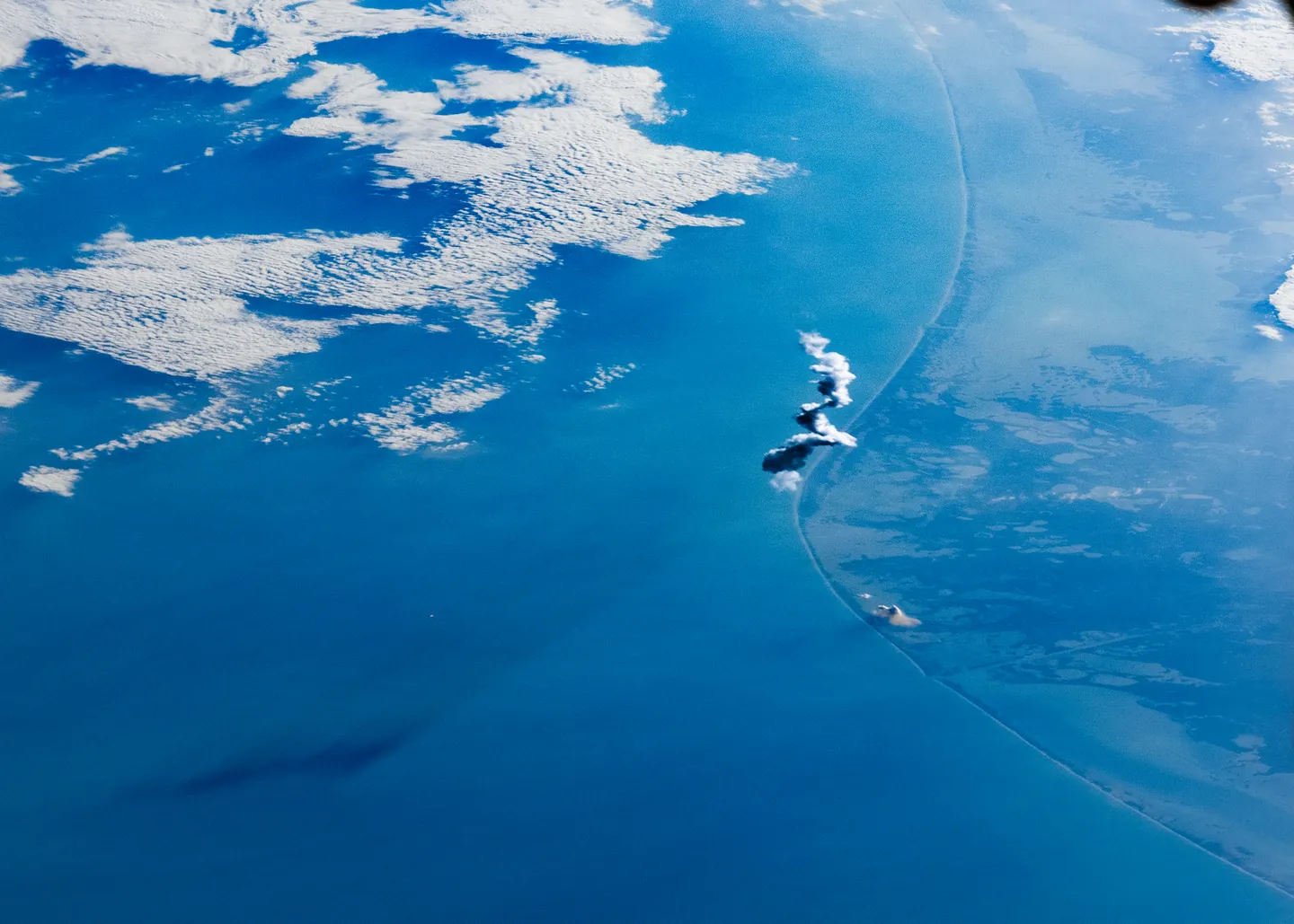 The Gulf coast seen from the International Space Station, with a white rocket plume rising above the sea